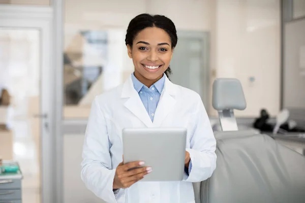 Lächelnde schwarze Zahnärztin mit digitalem Tablet posiert in Klinik für Stomatologie — Stockfoto