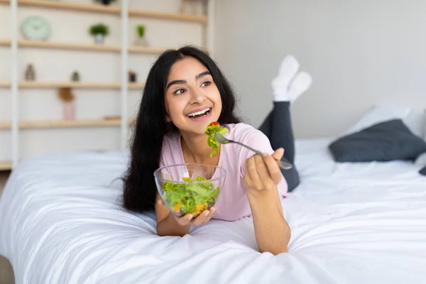 Weight loss diet concept. Pretty Indian woman eating fresh vegetable salad on bed at home, full length — Stock Photo, Image