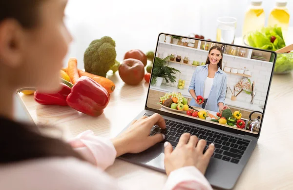 Young woman using laptop computer to take part in online culinary workshop, learning vegan cuisine recipes on web — Stock Photo, Image