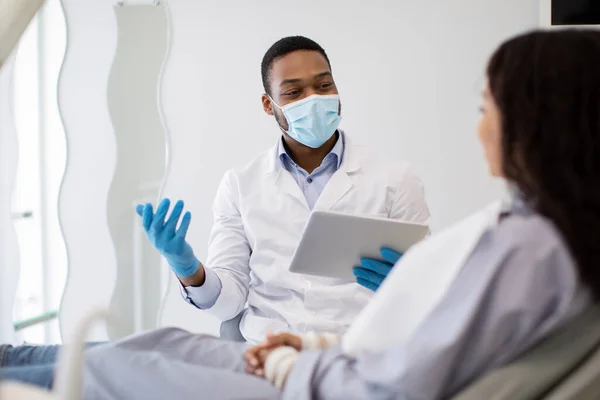 Μαύρος οδοντίατρος γιατρός με ψηφιακή ταμπλέτα στα χέρια παροχή συμβουλών ασθενή στην κλινική — Φωτογραφία Αρχείου