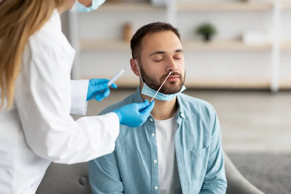 Doctor making covid-19 PCR test for male patient at home. Viral disease prevention and treatment concept — Stock Photo, Image