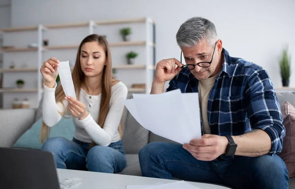 Family budget planning. Married mature couple with documents and bills counting their finances on laptop at home