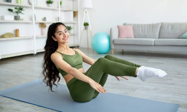 Positive athletic Indian woman doing abs exercises during her domestic workout, indoors — Foto de Stock