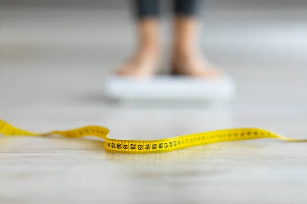 Measuring tape on floor and blurred view of millennial woman on scales, checking result of her slimming diet — Photo