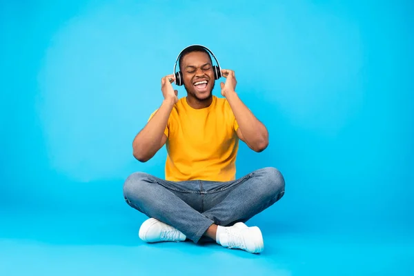 African American Guy Enjoying Music In Wireless Headphones, Blue Background