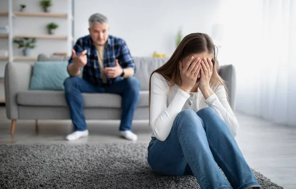 Emocjonalne nadużycie w małżeństwach. Dojrzała kobieta płacze na podłodze, mąż obwinia ją lub oskarża w domu — Zdjęcie stockowe