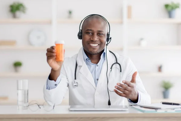 Een doktersaanbeveling. Gelukkig Afrikaans-Amerikaanse therapeut in witte jas tonen pot pillen, met online overleg — Stockfoto