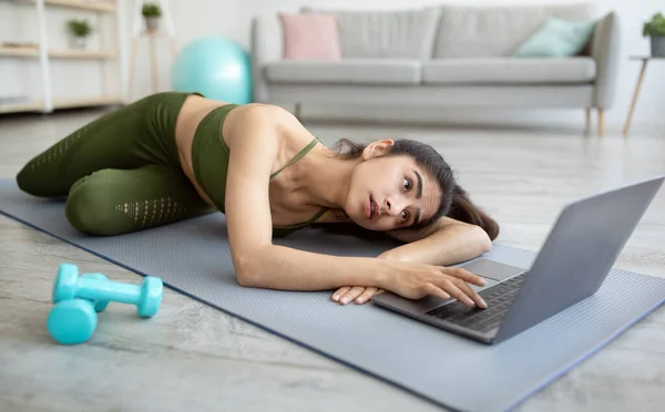 Online sporten. Uitgeputte jonge Indiase vrouw liggend op yoga mat in de buurt laptop, met geen kracht voor binnenlandse training — Stockfoto