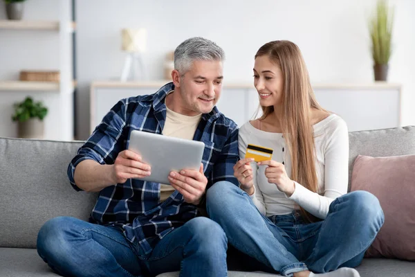 Online shopping concept. Cheerful mature couple using digital tablet and credit card together at home — Photo