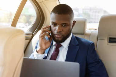 Businessman working on laptop, using smartphone while going to airport