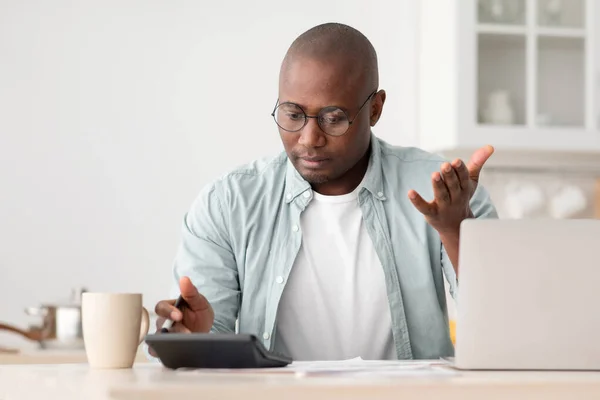 Savings and finances concept. Shocked black mature man calculating bills, using calculator, sitting in kitchen —  Fotos de Stock