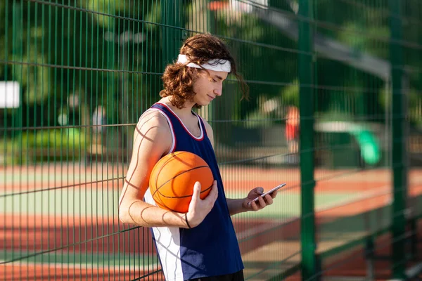 Young Caucasian basketball player using cellphone during game break at outdoor court — Stok Foto