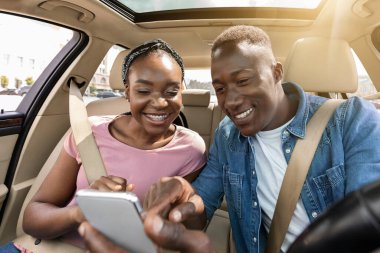 Smiling black man and woman using mobile phone in car