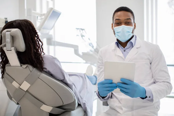 Чорний стоматолог лікар в медичній масці позує на робочому місці з цифровим планшетом — стокове фото