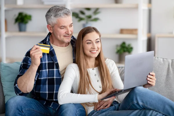 Easy online payment. Mature Caucasian couple holding credit card, using laptop pc, choosing and buying good on web — Stock Fotó