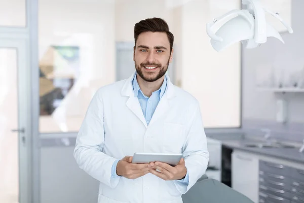 Delighted dentist smiling and holding digital tablet in dental cabinet — Φωτογραφία Αρχείου