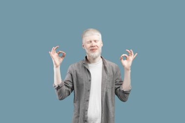 Great job. Excited albino man gesturing ok signs with both hands, showing that he is fine, blue studio background