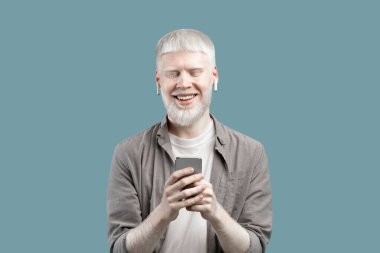People and technology concept. Excited albino man using smartphone, standing isolated over blue studio background