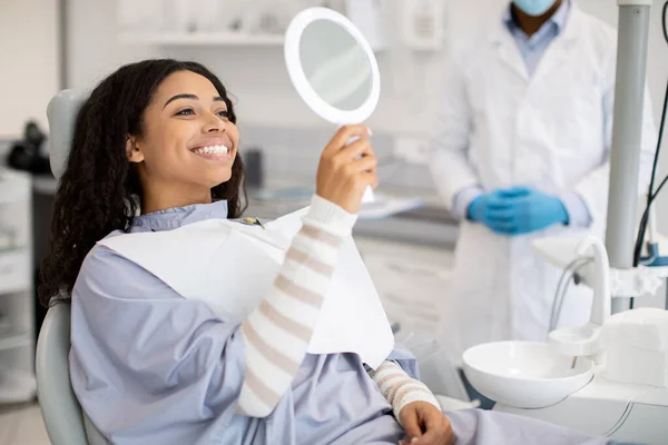 Happy Black Female Patient Looking At Mirror After Dental Treatment In Clinic — Foto de Stock