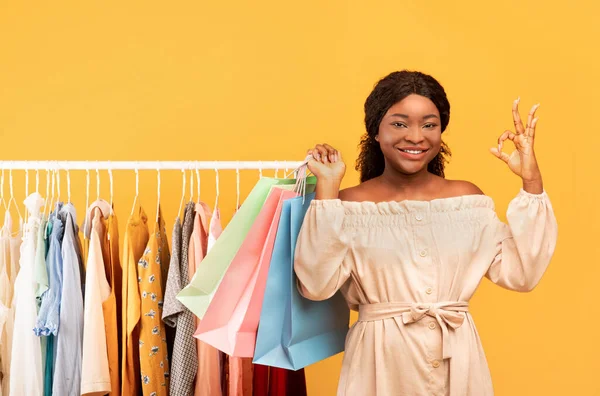 Happy black woman showing okay gesture near clothing rack full of stylish clothes, shopping for summer wardrobe — Stok fotoğraf