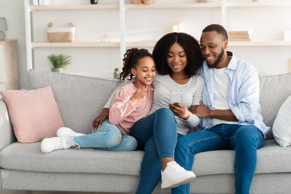 Happy african american family holding and using smartphone at home — ストック写真