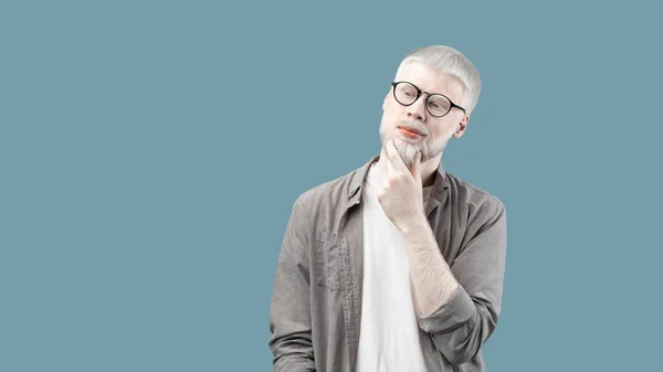 Thoughtful albino guy with unusual appearance touching chin and thinking about question, blue background, panorama — Stok fotoğraf