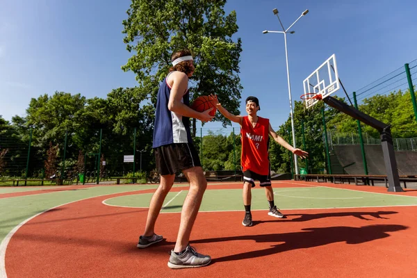 Two millennial sportsmen playing basketball match at outdoor playground, blank space — Stok Foto