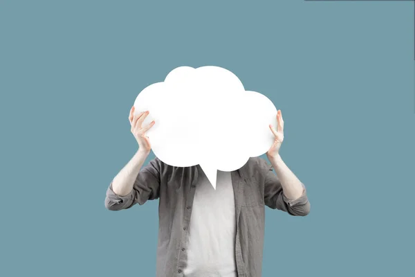 Unrecognizable young albino man holding blank speech bubble in front of his face over turquoise studio background — стоковое фото