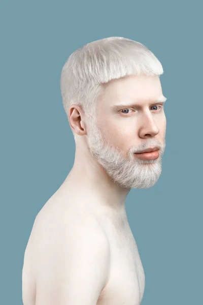 Безтурботний молодий альбінолог з блідою шкірою та білим волоссям, позує на камеру без сорочки на бірюзовому фоні — стокове фото