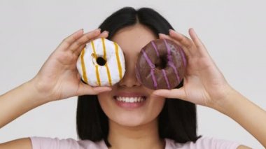 Donutla gözlerini kapayan Asyalı kadın eğleniyor, beyaz arka plan