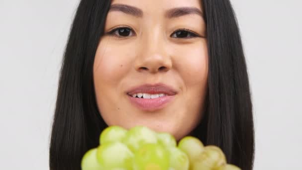 Senhora muito chinesa comendo uvas verdes sobre fundo branco estúdio — Vídeo de Stock