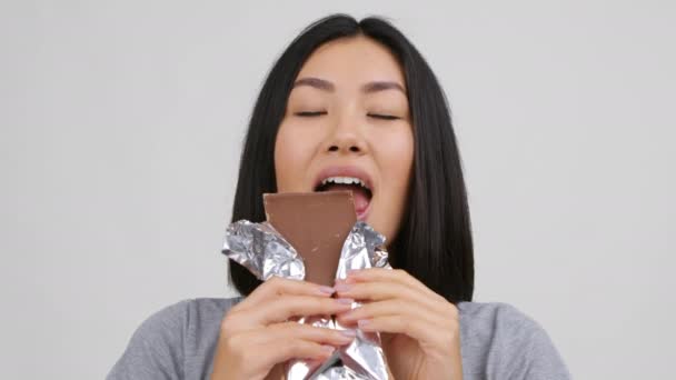 Щаслива китайська жінка їсть великий шоколад позує на білому тлі — стокове відео