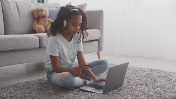 Linda niña afroamericana haciendo el pago por Internet, introduciendo información de la tarjeta de crédito en el ordenador portátil en casa — Vídeo de stock