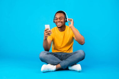 Afrikalı Adam Müzik Dinliyor Akıllı telefon kullanıyor Kulaklık takıyor, Mavi Arkaplan