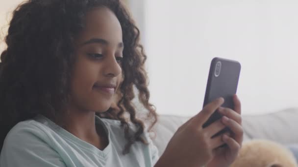 Primer plano retrato de adolescente afroamericana chica en red en el teléfono celular, jugando juegos o charlando con amigos en línea — Vídeo de stock