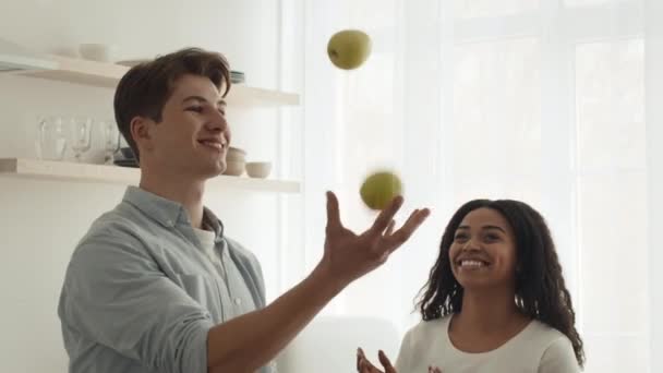 Vielfältiges Paar hat Spaß beim Kochen und Jonglieren mit Äpfeln in der Küche — Stockvideo
