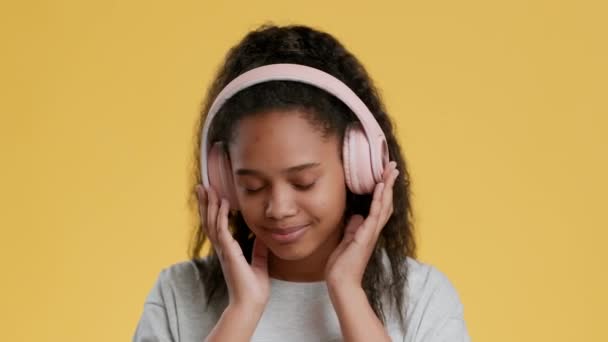 Teen hobby. Cute african american teenage girl listening to music in pink wireless headphones, enjoying great sound — Stock Video