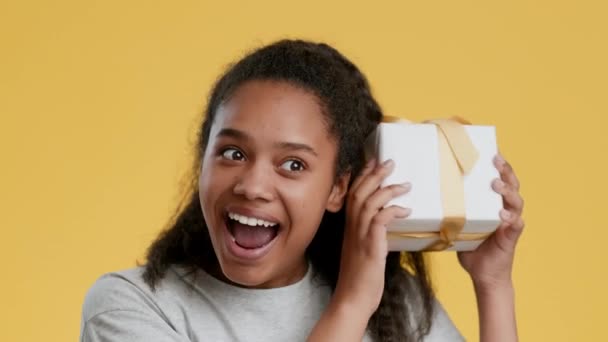 Vážený dárek. Šťastný africký americký dospívající dívka třesoucí dárkové krabice, snaží se hádat, co je uvnitř, pocit vzrušení — Stock video