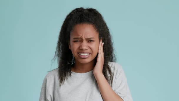 African american teen girl suffering from acute toothache, touching sore cheek and grimacing to camera, blue background — Stock Video