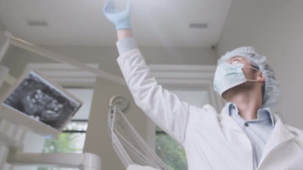 Στο οδοντιατρείο. Επαγγελματίας οδοντίατρος φορώντας προστατευτική μάσκα και γάντια ανάβοντας το φως και ξεκινήστε το τσεκάπ — Αρχείο Βίντεο