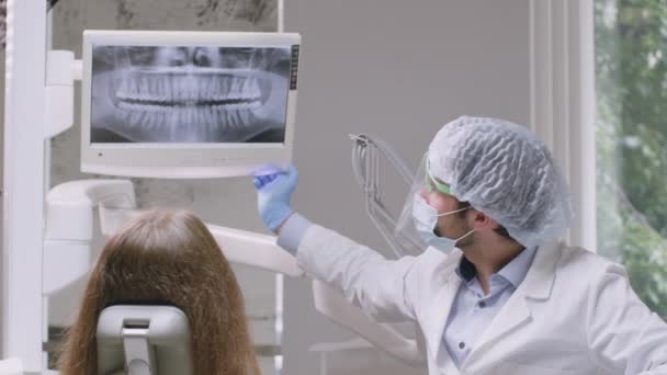 Επαγγελματίας οδοντίατρος που δείχνει ακτινογραφία στον ασθενή σε ψηφιακή οθόνη, συζητώντας σχέδιο θεραπείας, κάθεται στο γραφείο — Αρχείο Βίντεο