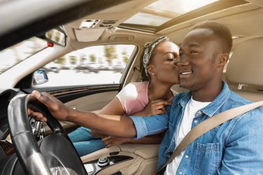 Arabayla seyahat ederken kocasını öpen siyahi bir kadın.