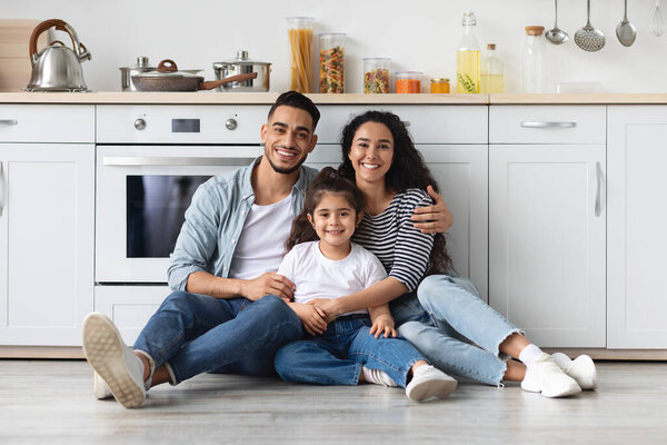 Beautiful middle-eastern family sitting on floor at kitchen