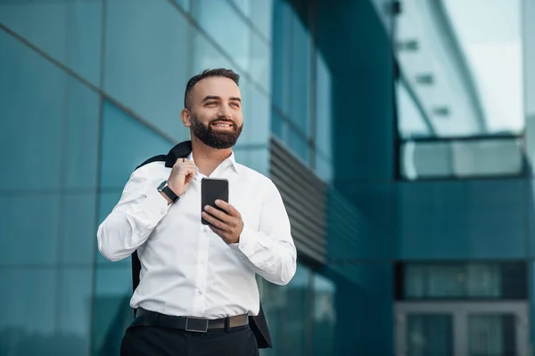 Yetişkin bir iş adamı ofis binasının yanında yürürken akıllı telefonunu kontrol ediyor ve yan tarafa bakıyor, boşluğu kopyalıyor. — Stok fotoğraf