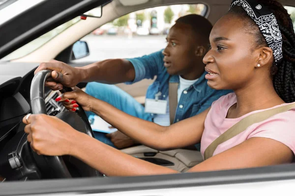 Nervous black lady attending driving school, driving with instructor