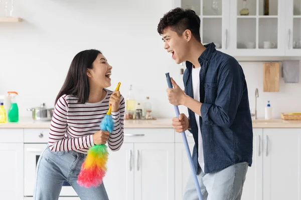 Funny asian man and woman singing songs while house-keeping — Stock Photo, Image