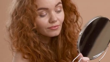 Kızıl saçlı kadın aynaya bakıyor Bej arkaplandaki saçlara dokunuyor