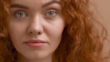 Kafası karışmış kızıl saçlı kadın bej arkaplan üzerine kaş kaldırıyor.