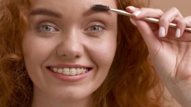 Bej Stüdyo Arkaplanı Üzerinde Kaşlarını Fırçalayan Çekici Kızıl Saçlı Kadın