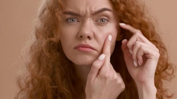 Concerned Red-Haired Young Woman Searching Eye Wrinkles Over Beige Background — Stock Video